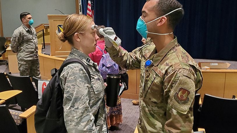 Airman 1st Class Luis Cintron, a dental technician at the Wright-Patterson Medical Center, takes a temperature reading from Capt. Kelsey Pruitt, a nurse practitioner with the Women’s Health Center as she arrives for duty March 25. All medical center staff members are now having their temperatures checked upon arriving at the facility for duty at one specified location. (U.S. Air Force photo/Bryan Ripple)