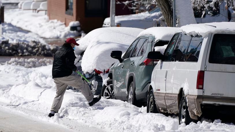 A motorist tries to clear snow to drive his van after a powerful late winter storm dumped more than 2 feet of snow Monday, March 15, 2021, in Denver. The storm shut down major roadways, canceled school and closed the state legislature. (AP Photo/David Zalubowski)