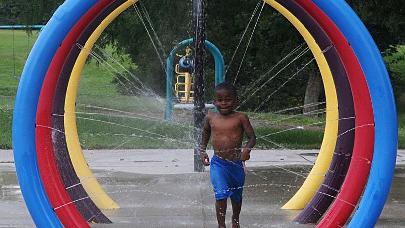 A boy beats the heat on a summer day by playing in a spray park along Germantown Street in Dayton. (Marshall Gorby/Staff)