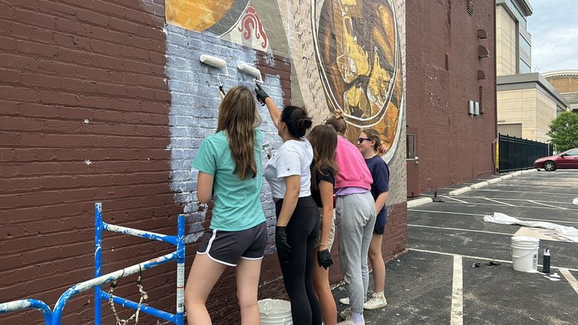 (left to right) Madison Coffee, Sahij Kaur, Molly Van Kirk-Butler, Lucia Skalicky Luqui and Julia Nielsen paint adhesive on the side of Mudlick Tap House. STAFF/ZOE HILL