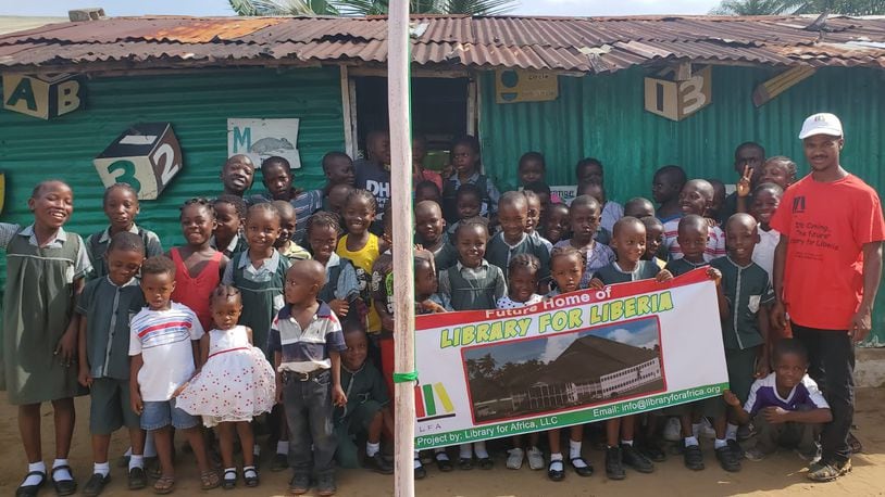 Co-Founder of Library for Africa, Darius Ricks, with students from Ardju Preparatory and Daycare Center holding a banner o the future Library of Liberia.