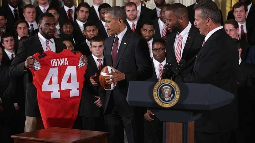 WASHINGTON, DC - APRIL 20: Doran Grant (L) of the Ohio State University Buckyes football team presents U.S. President Barack Obama (2nd L) a team jersey as teammate Curtis Grant (3rd L) and head coach Urban Meyer (R) look on during an East Room event at the White House April 20, 2015 in Washington, DC. President Obama hosted the football team to honor its victory on the first ever College Football Playoff National Championship. (Photo by Alex Wong/Getty Images)