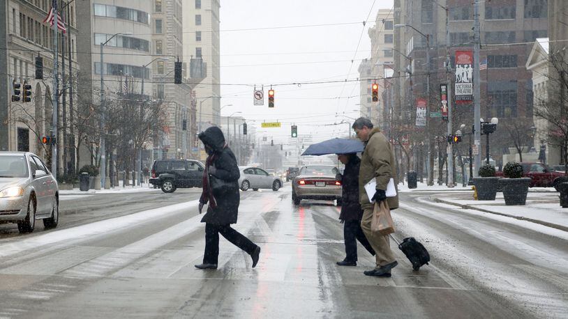 Pedestrians make their way through downtown Dayton as snow falls across the Miami Valley. LISA POWELL / STAFF FILE
