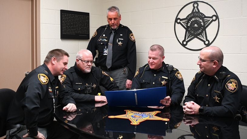 Miami County sheriff's department representatives, including Sheriff Dave Duchak (standing), review the manual for the Protect the Protectors brain health project used by the department and the county Communication Center. CONTRIBUTED