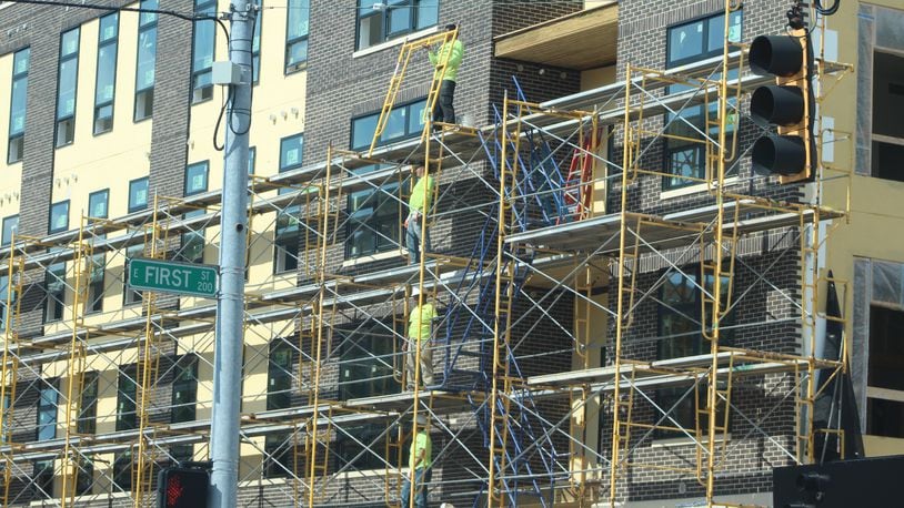 Construction crews work on the exterior of a new apartment building in downtown Dayton called the Sutton. CORNELIUS FROLIK / STAFF