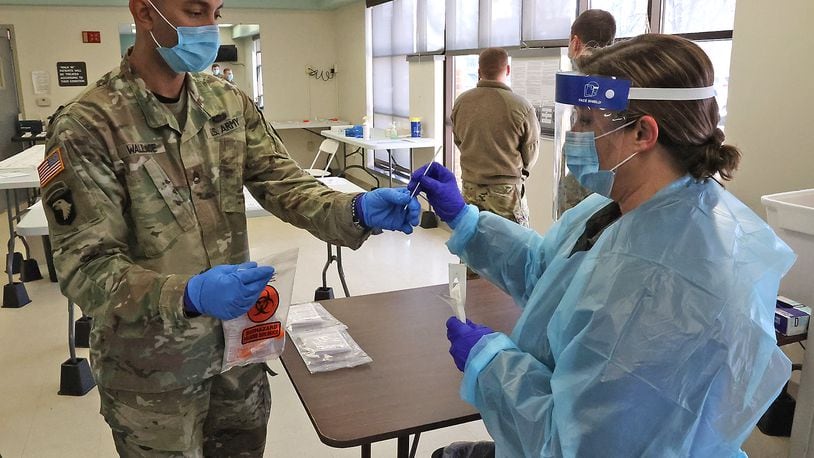 Renee Steele, from the Clark County Combined Health District, hands off a COVID test to SFC David Wallace of the Army National Guard so he can check it Tuesday at the COVID Testing Center on East High Street. BILL LACKEY/STAFF
