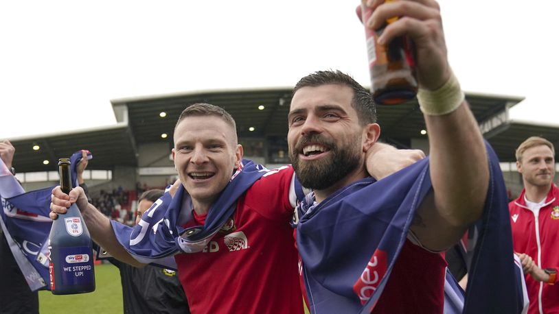 Wrexham's Paul Mullin and Elliot Lee on the pitch celebrating promotion to League One after the final whistle of the Sky Bet League Two match at the SToK Cae Ras, Wrexham, Saturday April 13, 2024. (Jacob King/PA via AP)