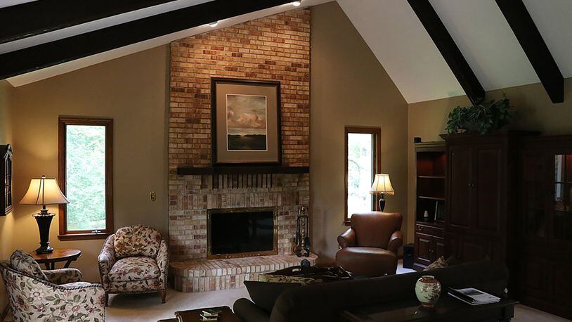 Under a beamed cathedral ceiling, brick facing surrounds the great room’s fireplace from the raised hearth to the angled ceiling. A wood-framed atrium door and window connect to the patio.