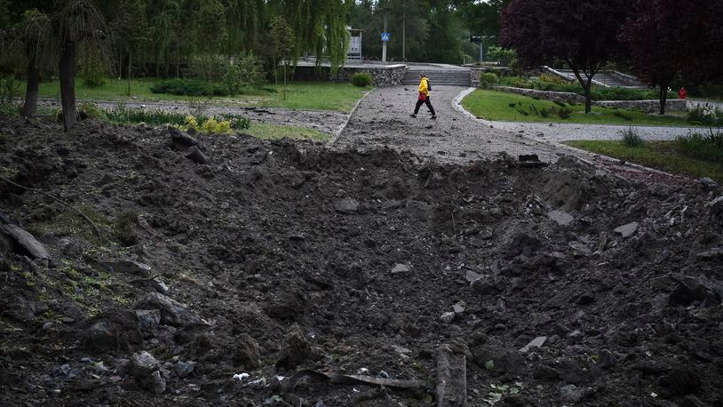 A woman walks in front of a crater caused by a Russian missile attack in Zaporizhzhia, Ukraine, Wednesday, May 8, 2024. (AP Photo/Andriy Andriyenko)