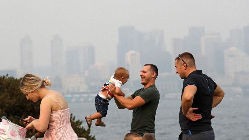 A man twirls a young child on a waterfront park as downtown Seattle disappears in a smoky haze behind, Sunday, Aug. 19, 2018. (AP Photo/Elaine Thompson)