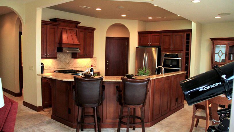 A large island provides seating around the kitchen space. Granite covers the tiered counter above a matching work counter below it.