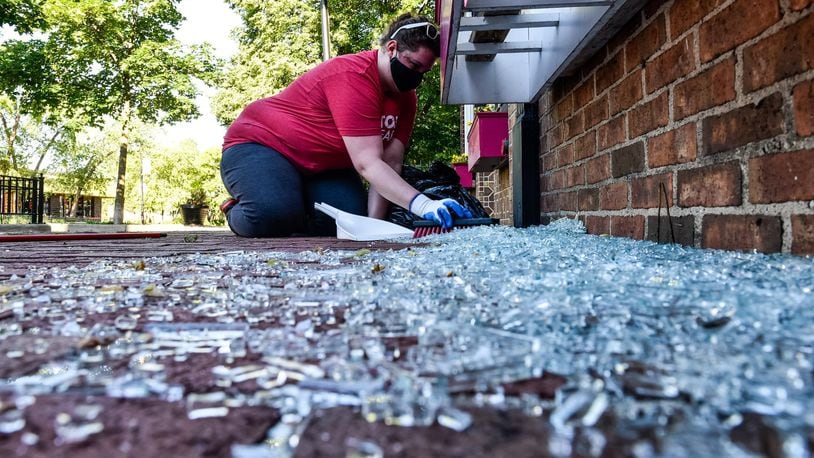 Jordan Buffington, from Beavercreek, cleans up glass from a broken window at Lily’s Bistro Sunday morning in the Oregon District. Signs, debris and graffiti damage were left in downtown Dayton Sunday morning, May 31, after protests throughout the day on Saturday in the aftermath of the death of George Floyd. CIty and county workers, business owners and volunteers spent the morning sweeping up glass and scrubbing spray paint. NICK GRAHAM / STAFF