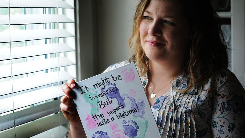 Bethany Sibbitt, a Montgomery County foster caregiver, holds a painting that features the tiny footprints of the infant in her care.  MARSHALL GORBY\STAFF