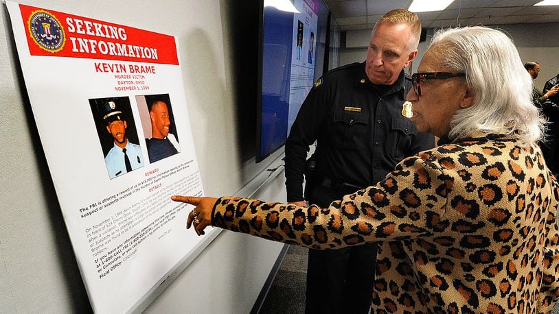 Rosemary Brame, mother of Dayton police officer Kevin Brame who was gunned down in November 1999, points to an FBI poster with Maj. Brian Johns of the Dayton Police Department after a Thursday, April 11, 2024, press conference at the Dayton Safety building. MARSHALL GORBY\STAFF