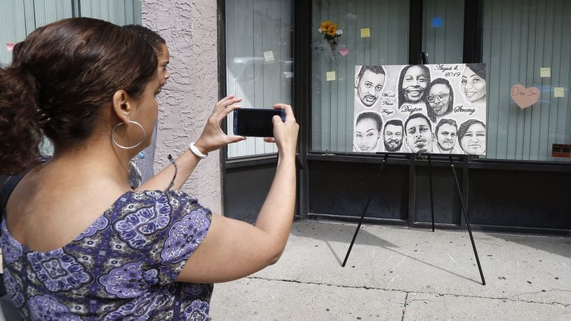 Native Daytonian Christi Colbert takes a picture of a new portrait that is on display in the Oregon District with the faces of the nine shooting victims painted by Abby Kaiser. Colbert was back in town from her current home in Maryland and visited East Fifth Street on Friday afternoon. TY GREENLEES / STAFF