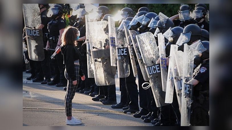 A girl stands in front of Dayton police officers in riot gear during protests Saturday, May 30, 2020, in Dayton. MARSHALL GORBY / STAFF