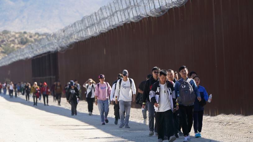 FILE - A group of people, including many from China, walk along the wall after crossing the border with Mexico to seek asylum, Oct. 24, 2023, near Jacumba, Calif. Beijing and Washington have quietly resumed cooperation on the deportation of Chinese immigrants who are in the U.S. illegally, as the two countries are reestablishing and widening contacts following their leaders' meeting in California late 2023. (AP Photo/Gregory Bull, File)