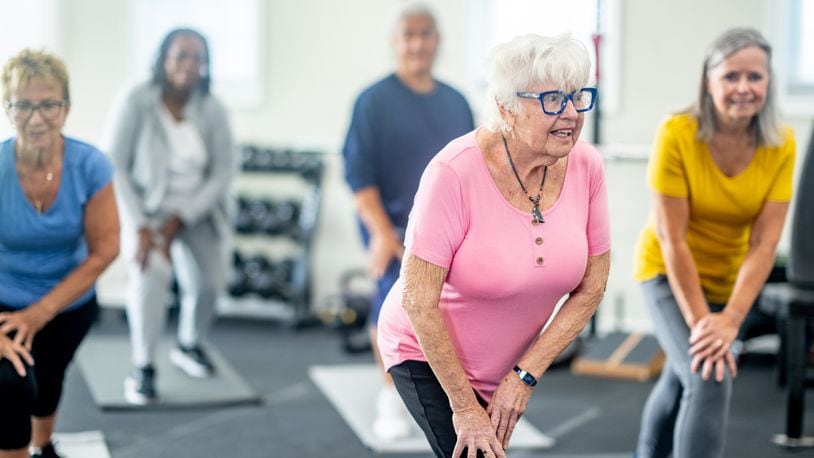 A small group of diverse seniors work out in a small fitness studio together. They are each dressed comfortably as they hold a stretch and focus on their breathing. CREDIT: FATCAMERA/ISTOCK