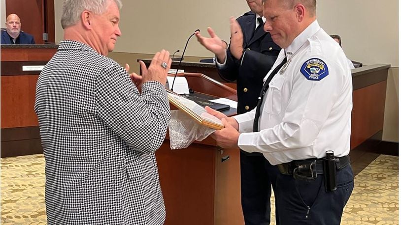 Springboro Mayor John Agenbroad, left, and Police Chief Dan Bentley, center, lead the audience in applause for Officer Christopher Heath Martin being awarded the city's Life Saving Commendation during Thursday's Springboro City Council meeting. On June 23, Martin responded to a house fire where a disabled man was trapped. Martin crawled on his hands and knees to find the man in a burning bedroom and get him to safety. ED RICHTER/STAFF