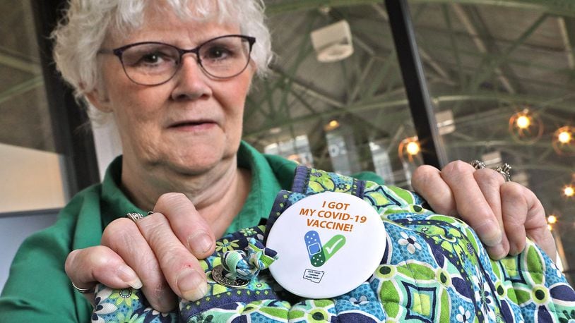 Linda Gast shows the COVID-19 vaccine button she wears on her backpack Tuesday, August 30, 2022. Since contracting COVID and dealing with it's effects for the past two years, she encourages everyone to get vaccinated. BILL LACKEY/STAFF