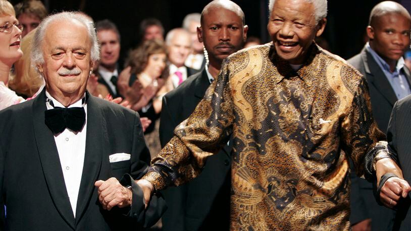 FILE — In this Wednesday Nov. 12, 2008 file photo George Bizos, left, anti-apartheid activist, and life-long friend and lawyer of Nelson Mandela, right, arrives for his 80th birthday party in Johannesburg, South Africa. Bizos has died Wednesday Sept. Sept. 9, 2020, aged 92. (AP Photo/Denis Farrell)