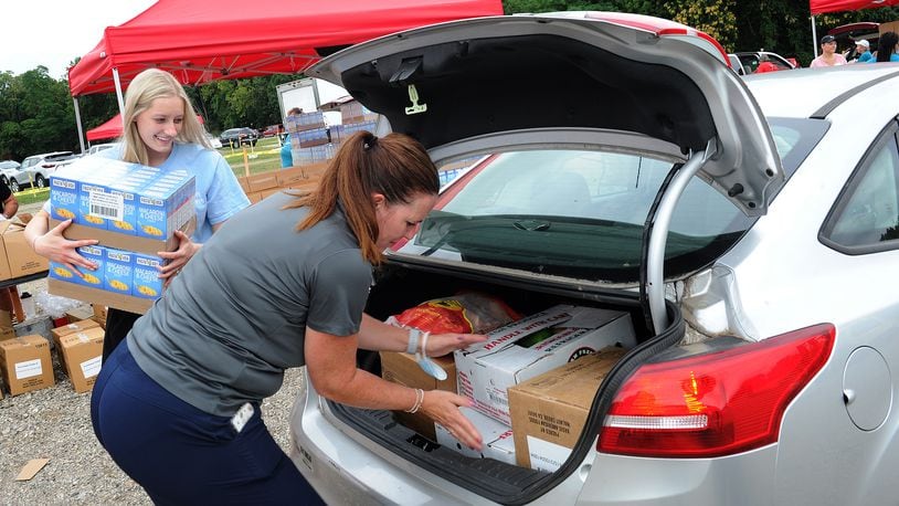 Ashtyn Grabtree, left, and Bridgett Hobbs loads food into the trunk of a car Tuesday Aug. 16, 2021, during the mass drive-thur food distribution at the Dixie Twin Drive-In hosted by the Foodbank. MARSHALL GORBY\STAFF