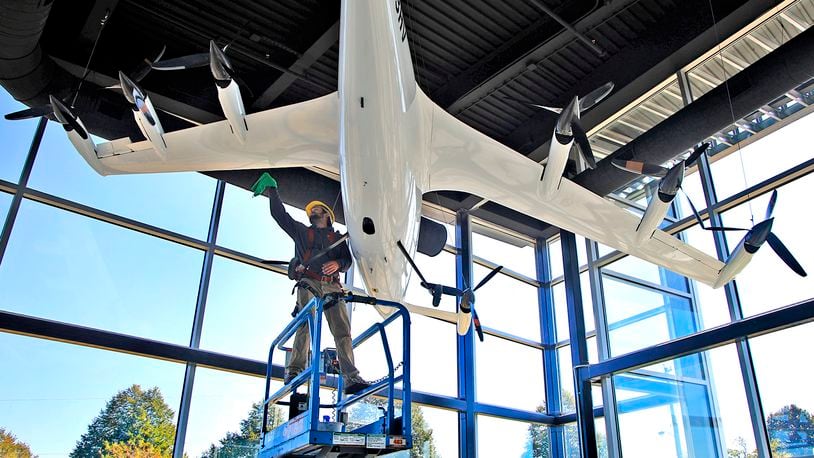 Owen Flannery, an employee with the City of Springfield, cleans the electric vertical take off and landing aircraft that hangs in the lobby of the new National Advanced Air Mobility Center of Excellence at Springfield-Beckley Municipal Airport Thursday, Sept. 14, 2023. BILL LACKEY/STAFF