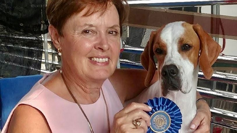 Dr. Patricia Haines smiles posing with a blue ribbon and a brown and white Pointer dog.