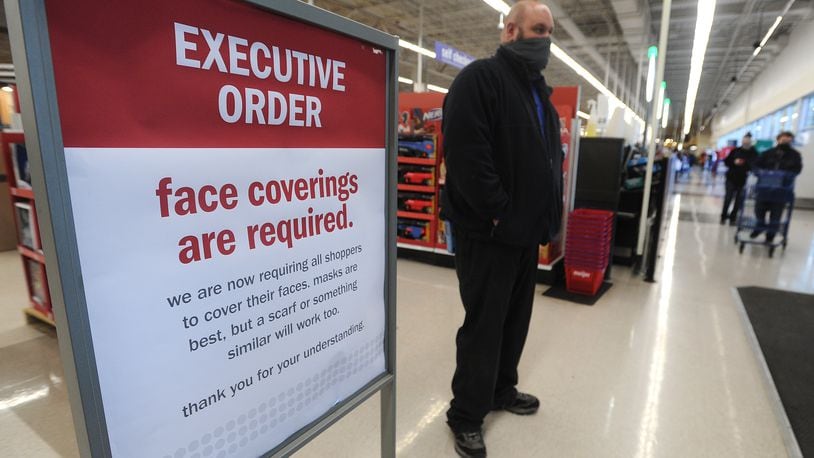 Meijer meat team leader, Tyler Winthrop, stands next to one of the executive order signs at the entrance to the Meijer store on Wilmington Pike Monday. Winthrop said, that all customers have been very compliant to the order.  MARSHALL GORBY\STAFF