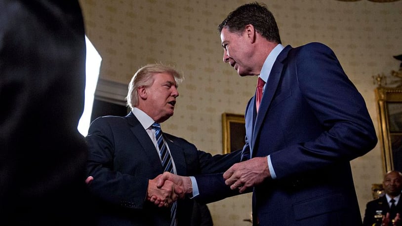 U.S. President Donald Trump (C) shakes hands with James Comey, director of the Federal Bureau of Investigation (FBI), during an Inaugural Law Enforcement Officers and First Responders Reception in the Blue Room of the White House on January 22, 2017 in Washington, DC. Trump today mocked protesters who gathered for large demonstrations across the U.S. and the world on Saturday to signal discontent with his leadership, but later offered a more conciliatory tone, saying he recognized such marches as a "hallmark of our democracy." (Photo by Andrew Harrer-Pool/Getty Images)