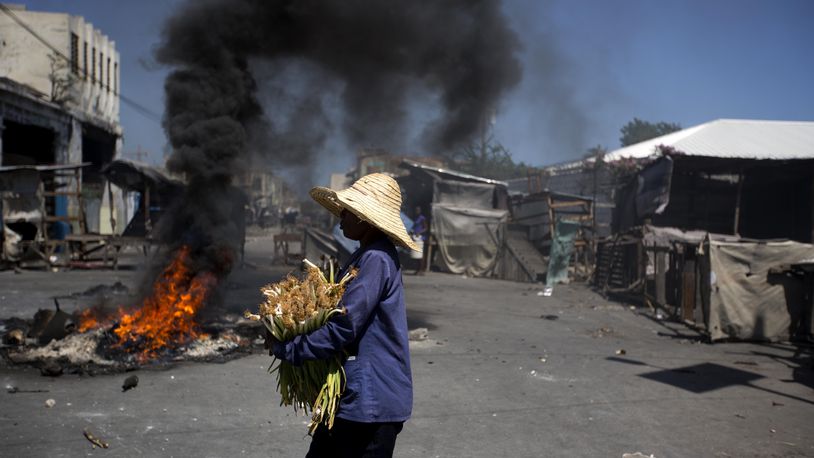 A street vendor walks past burning tires set up by anti-government protesters during a general strike in Port-au-Prince, Haiti, Monday, July 9, 2018. A nationwide, general strike and protest was called to demand the resignation of Haiti's President after his government agreed to reduce subsidies for fuel. The fuel hike was suspended after widespread, violent protests broke out on Friday and over the weekend.