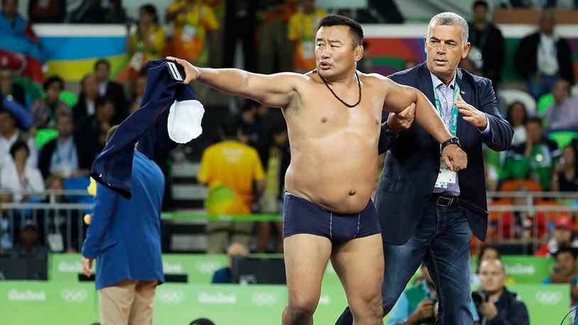A coach of Mongolia’s wrestler Mandakhnaran Ganzorig take off their clothes in protest against the decision of the jury to award the bronze medal to Uzbekistan’s Ikhtiyor Navruzov during the men’s 65-kg freestyle wrestling competition at the 2016 Summer Olympics in Rio de Janeiro, Brazil, Sunday, Aug. 21, 2016. (AP Photo/Markus Schreiber)
