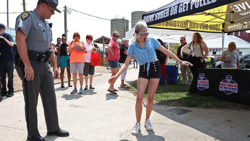 Lt Brian Aller of the Ohio State Highway Patrol has a woman perform a basic sobriety test while wearing impaired driving goggles Tuesday during the Drive Sober or Get Pulled Over kick-off at Young's Jersey Dairy. BILL LACKEY/STAFF