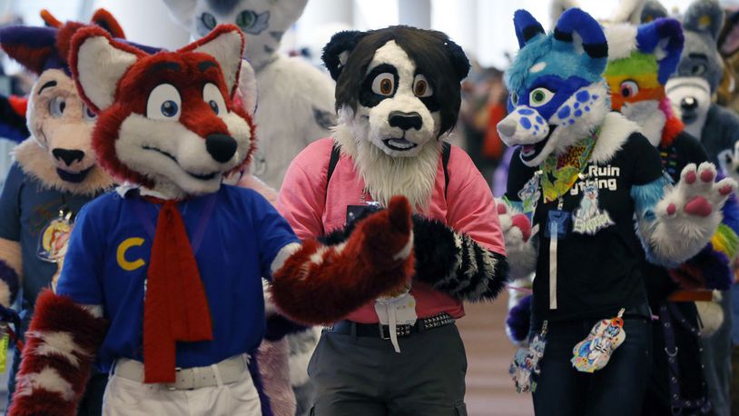 A few of the participants in the annual Anthrocon convention wave to other enthusiasts as they parade through Pittsburgh's David Lawrence Convention Center after they posed for a photograph in an attempt to set a Guinness World Record with the number of individuals gathered at one time in what they call full firsuit attire on Saturday, July 6, 2013, in Pittsburgh.
