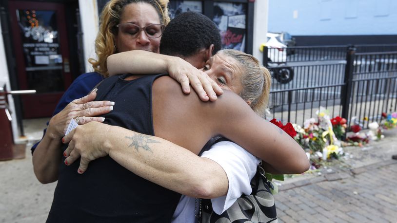 Harry Payne is hugged by Jean Davies, left, and Mary K. Curtis as he arrived on East Fifth Street on Monday to leave flower for his slain friend Logan Turner who was gunned down early Sunday morning with seven other victims. TY GREENLEES / STAFF