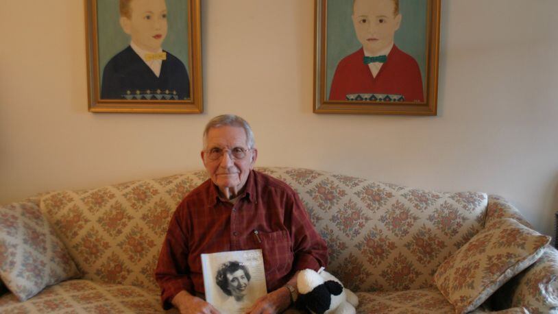 Bob Lamb in his Centerville home, holding a copy of “A Kiss on the Magic Spot,” a compilation of works by his late wife, Jean. The portraits on the wall, painted by Jean, show their first two children, (from left) Kevin and Larry. The stuffed-animal lamb on the couch is also one of her creations. PAMELA DILLON/CONTRIBUTED