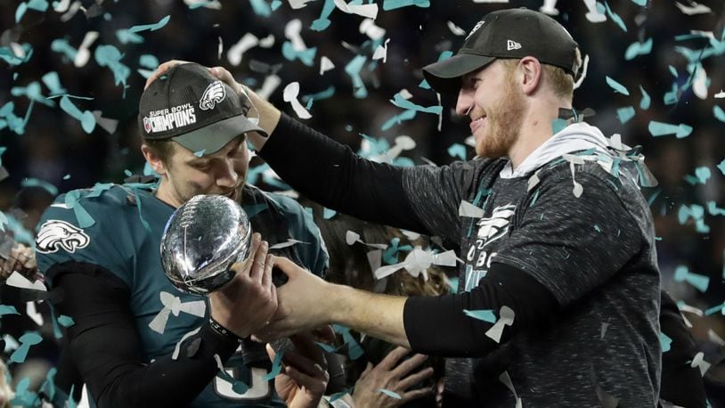 In this Feb. 4, 2018 photo, Philadelphia Eagles quarterback Carson Wentz, right, hands the Vincent Lombardi trophy to Nick Foles after winning the NFL Super Bowl 52 football game against the New England Patriots in Minneapolis. The Eagles won 41-33. President Donald Trump has called off a visit by the Philadelphia Eagles to the White House Tuesday due to the dispute over whether NFL players must stand during the playing of the national anthem.