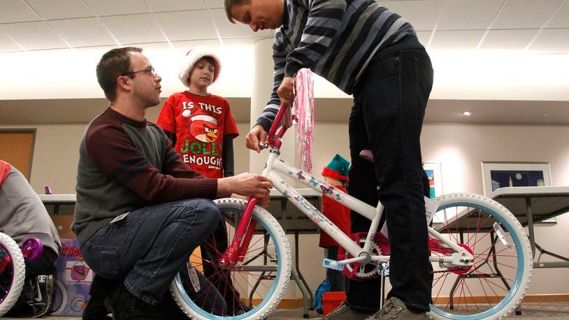 Reynolds and Reynolds’ annual bike-build event is Saturday. In this 2014 photo, Chris Brown (left) and co-worker Matt Owens (right) assemble a bike with the help of Owen’s son Aidan, then 11. LISA POWELL / STAFF PHOTO