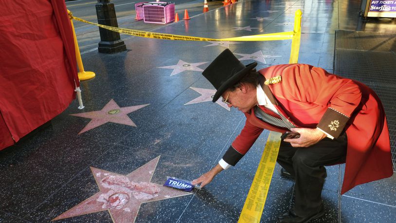 Gregg Donovan, who calls himself the unofficial ambassador of Hollywood, places a sticker for Republican presidential candidate Donald Trump on Trump's vandalized star on the Hollywood Walk of Fame, Wednesday, Oct. 26, 2016 in Los Angeles. Det. Meghan Aguilar said investigators were called to the scene before dawn Wednesday following reports that Trump's star was destroyed by blows from a hammer. (AP Photo/Richard Vogel)