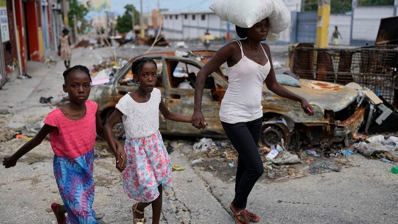 Residents walk past a burnt car blocking the street as they evacuate the Delmas 22 neighborhood to escape gang violence in Port-au-Prince, Haiti, Thursday, May 2, 2024. (AP Photo/Ramon Espinosa)