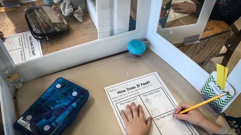First-grade students at Kettering's Orchard Park Elementary School do their work with protective plastic around their desks Tuesday, March 2, 2021. STAFF / JIM NOELKER