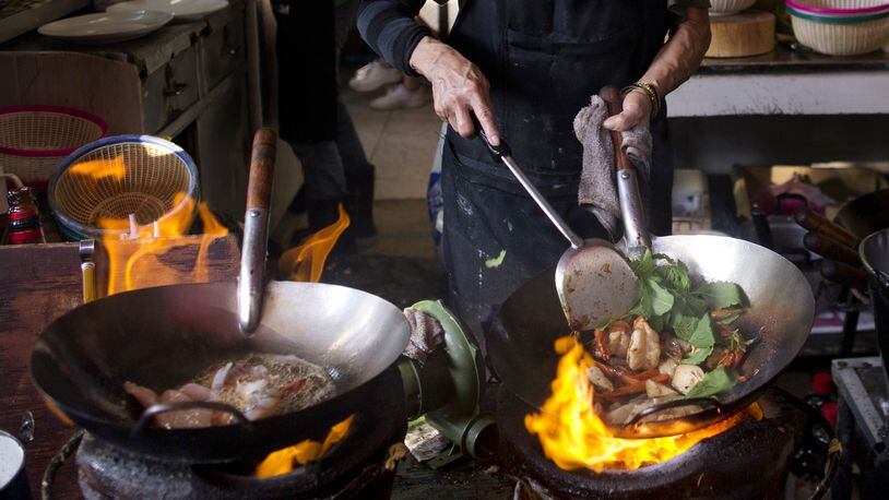In this Dec. 20, 2017, photo, Thai cook Supinya Jansuta, 72, better known as "Jay Fai," wearing goggles, cooks with two flaming woks at her eatery in Bangkok, Thailand. After spending more than three decades cooking in an unassuming outdoor kitchen, Jay Fay has been propelled to international culinary stardom by having her restaurant awarded a Michelin star.(AP Photo/Gemunu Amarasinghe)