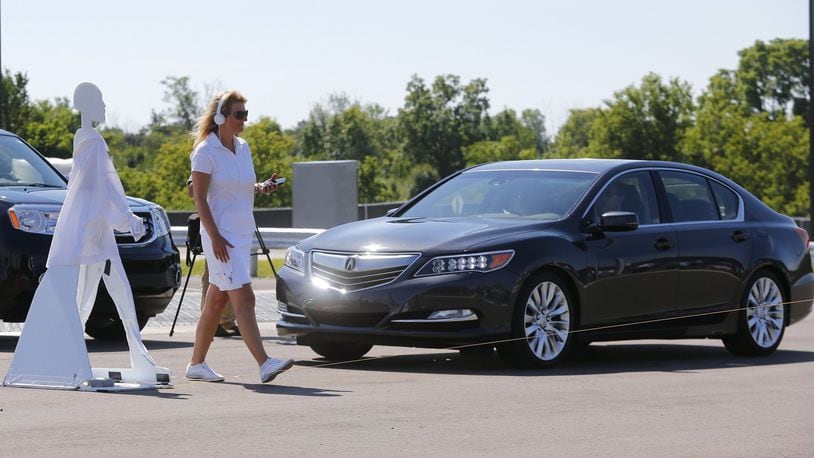 In this July 20, 2015 file photo, a pedestrian crosses in front of a vehicle as part of a demonstration at Mcity on its opening day on the University of Michigan campus in Ann Arbor, Michigan. Cars that wirelessly talk to each other are finally ready for the road, creating the potential to dramatically reduce traffic deaths, improve the safety of self-driving cars and someday maybe even help solve traffic jams, automakers and government officials say. (AP Photo/Paul Sancya, File)