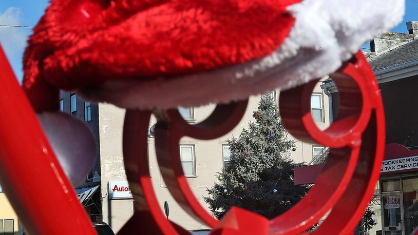 The New Carlisle Christmas tree is seen through a sculpture in front of Penny Lane Cafe and Art Gallery on Main Street Friday. New Carlisle will have an official tree lighting ceremony Saturday evening at 6:30pm. At the same time they will be lighting a minorah in memory of the vicitms of the Pittsburgh synagogue shooting. BILL LACKEY/STAFF