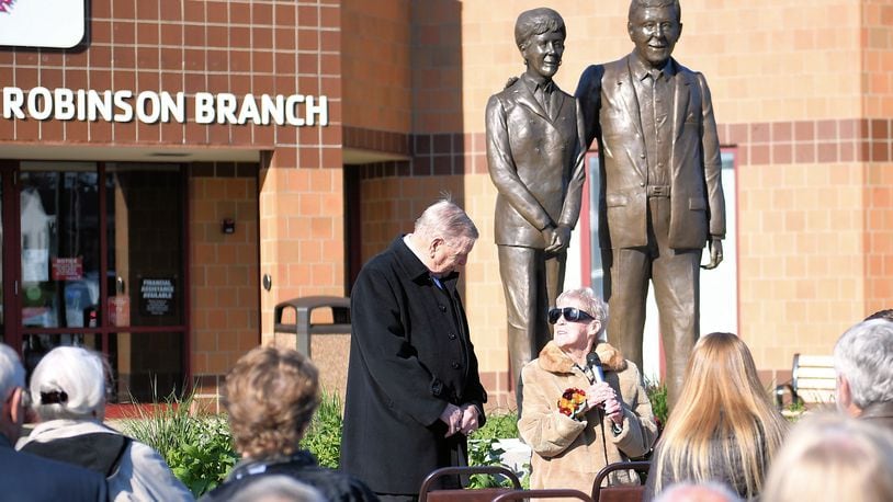 Thom Robinson (standing) and Pat Robinson (seated with microphone) address those attending the unveiling of sculptures of the Troy philanthropists at the Miami County YMCA Robinson Branch on Nov. 5. CONTRIBUTED