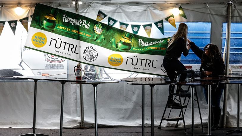 From left, Holly Pierce and Stephanie Markham hang banners in a large tent at Flanagan's Pub Thursday, March 16, 2023, in preparation of St. Patrick's Day. JIM NOELKER/STAFF