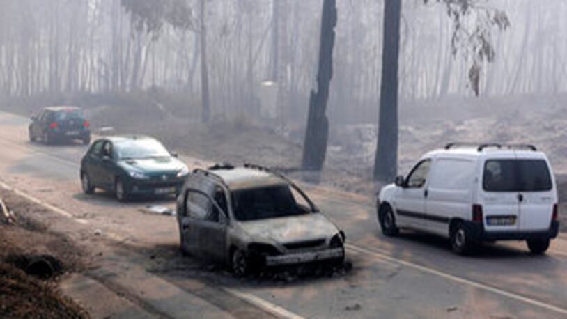 Cars drive past a burnt car on the road between Castanheira de Pera and Figueiro dos Vinhos, central Portugal, Sunday, June 18 2017.  Raging forest fires in central Portugal killed more than 50 people, many of them trapped in their cars as flames swept over a road, in what the prime minister on Sunday called "the biggest tragedy of human life that we have known in years". (AP Photo/Armando Franca),