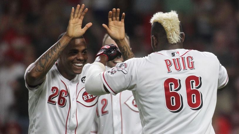 The Reds’ Raisel Iglesias, left, slaps hands with Yasiel Puig after Puig scored the winning run in the 11th inning against the Brewers earlier this month at Great American Ball Park in Cincinnati. David Jablonski/Staff