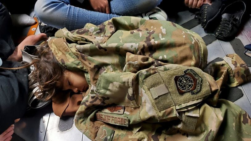 An Afghan child sleeps on the cargo floor of a U.S. Air Force C-17 Globemaster III, kept warm by the uniform of the C-17 loadmaster, during an evacuation flight from Kabul, Afghanistan, Aug. 15, 2021. Operating a fleet of Air National Guard, Air Force Reserve and Active Duty C-17s, Air Mobility Command, in support of the Department of Defense, moved forces into theater to facilitate the safe departure and relocation of U.S. citizens, Special Immigration Visa recipients, and vulnerable Afghan populations from Afghanistan. (U.S. Air Force Courtesy Photo)