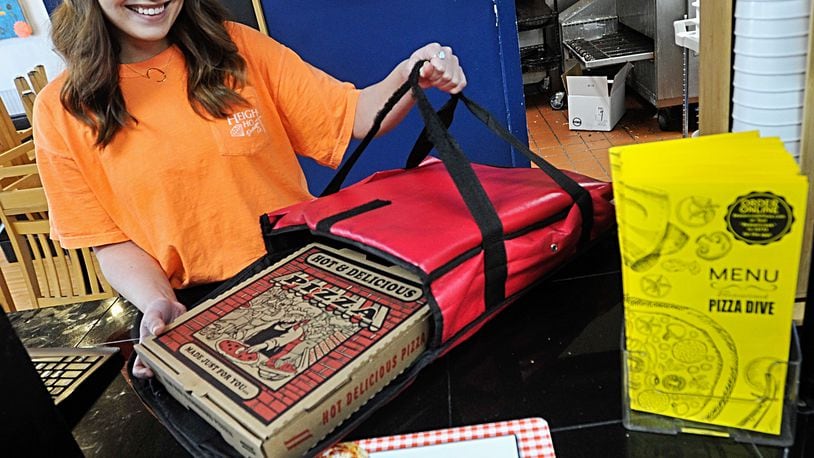Olivia Baker, and employee of Beavercreek Pizza Dive loads pizza into a warming bag to delivered Monday. Baker will Leave the pizza outside the door, ring the doorbell go back to her car and call and tell the customers their pizza is there. This will avoid all human contact. MARSHALL GORBYSTAFF